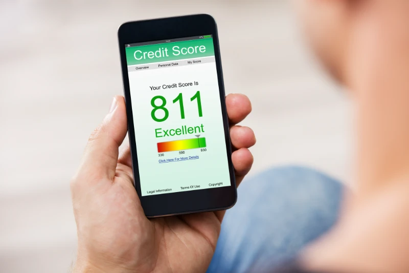 A person holds a smartphone displaying a credit score of 811, labeled as Excellent, on a green-themed screen with a score range and navigation tabs visible at the top.